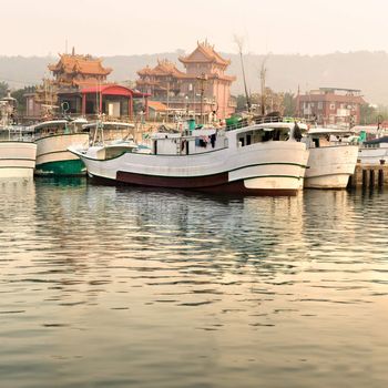 Boats in harbor with Chinese temple in morning.