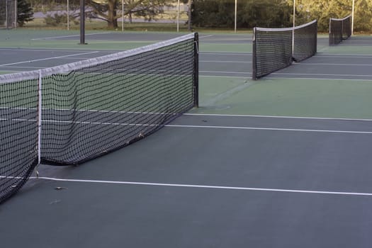 public tennis courts with green hard surface surrounded by park