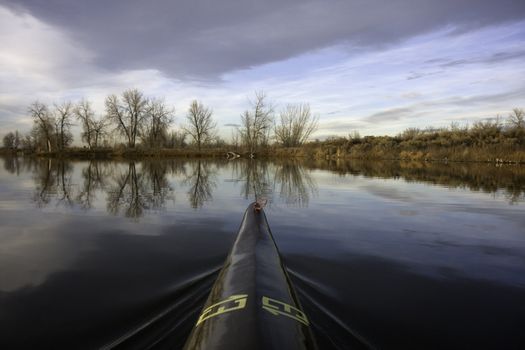 bow of a slim racing kayak (carbon fiber construction) with a temporary race number thirteen on a calm lake in late fall scenery