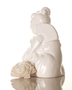 A ceramic geisha girl with white wooden flower isolated on white with reflection