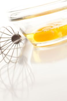 Hand Mixer with Eggs in a Glass Bowl on a Reflective White Background.