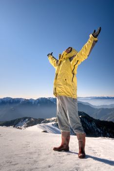 Man with open arms stand on snow mountain top.