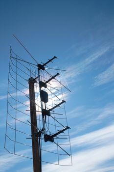 aerial TV antenna on rooftop over blue sky and sun