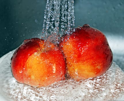 two fresh peaches close up under water in kitchen