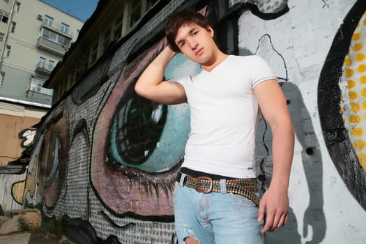 lad standing in torn jeans  near wall with graffiti
