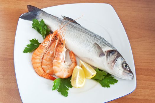 plate with sea bass, prawns, lemon and parsley isolated on wooden background
