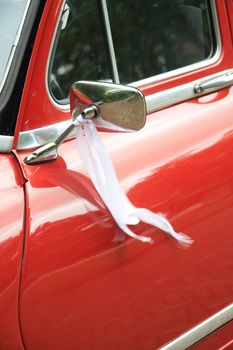 A red vintage car has a white ribbon on its mirror when serving as a wedding car