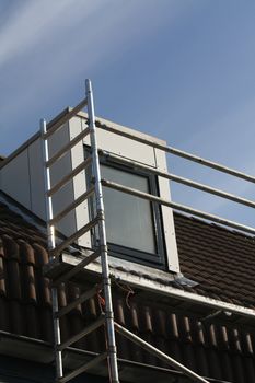 A scaffolding almost reaches the roof while a painter is busy with the windows