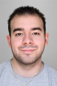 A headshot of a young guy that is smiling isolated on a gray background.