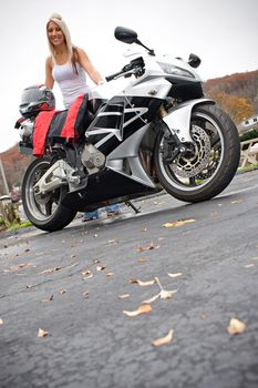 A pretty blonde woman posing with her motorcycle and riding gear.