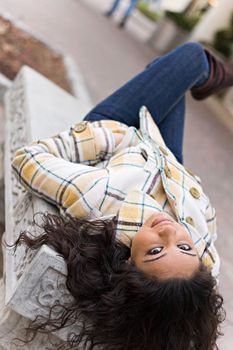 A closeup of a pretty Indian woman laying on a bench outdoors.