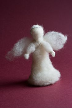 Handmade white wool angel on red background.