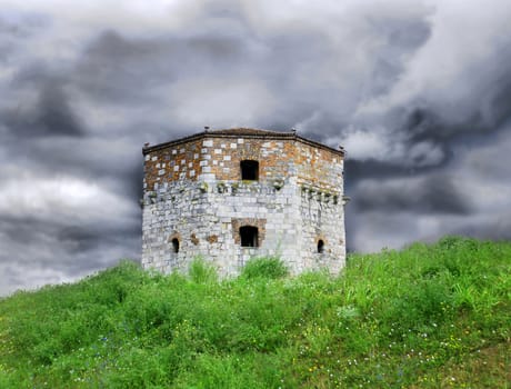 Old tower of Belgrade fortress on green hill over storming sky