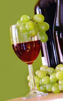 Red wine glass with grape and bottle over green