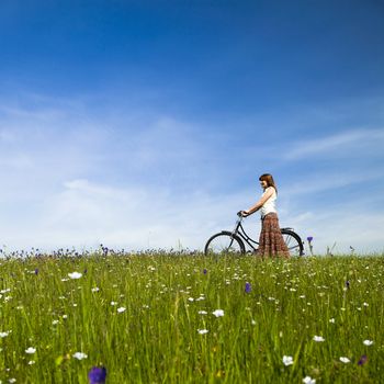 Happy young woman with a vintage bicycle on a green meadow