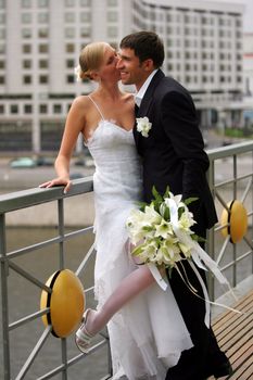 Close up of newlywed couple leaning against railing by water in urban scene.