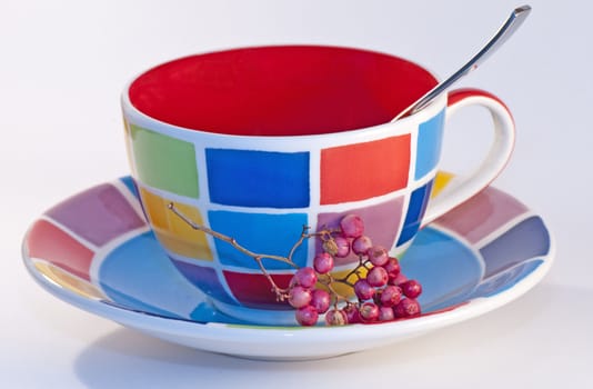 Colorful checkered cup with plate and silver spoon on a white background.