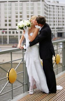 Newlywed couple kissing in urban scene, water in background.