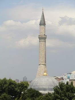 minaret against cloudy sky, cupula and trees in the foreground