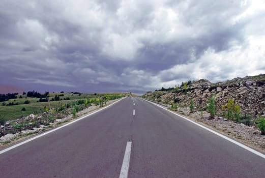 gray road through mountain landscape under cloudy sky