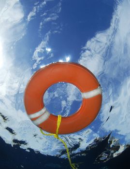 A survivor's perspective of a lifesaving ring landing on the surface of the water above them, with the distorted view of a blue cloudscape and the rescue boat above.