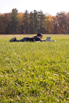 A young student using her laptop computer while laying in a green grassy field.