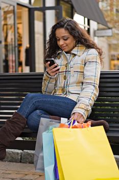 An attractive young woman checking her cell phone while out shopping in the city.