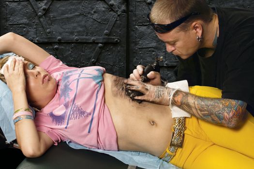 A tattoo artist applying his craft onto the abdomen of a female. (Property release supplied includes tattooists' art and his studio.)

