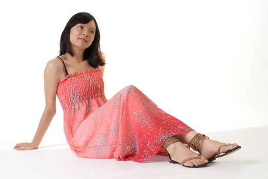 Oriental girl sit on ground in pink dress isolated on white background.