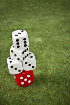 Piled dice on a red one over a green carpet