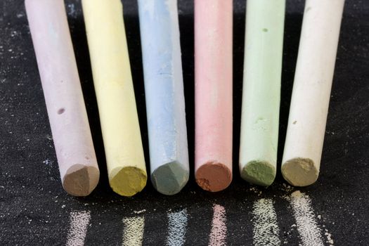 6 chalk sticks of different colors on a blackboard, focus on tips