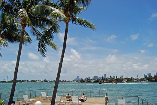 Couple sunbathing and relaxing on a condominium sundeck on the shores of biscayne bay with the Miami skyline in the distance.