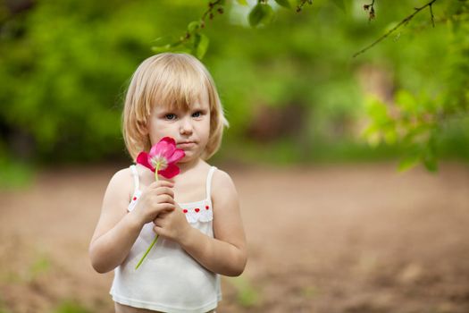 small serious girl with tulip outdoors in sunny day