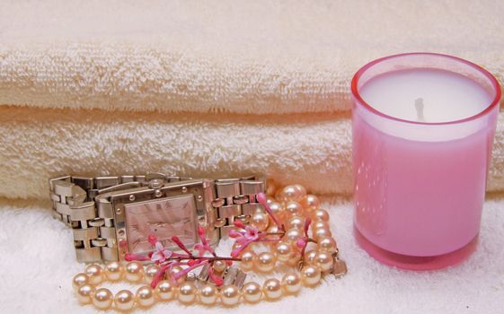 A watch, pearl necklace and a candle in front of towels