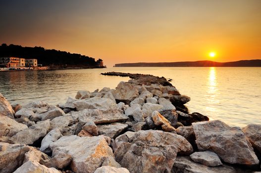 Image of a sunset in the town of Pylos, southern Greece, with rocks in the foreground and the island of Sfaktiria in the background