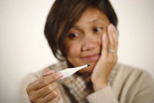 Asian female checking the temperature on a digital thermometer.  Women is out of focus - focus is on her hand and thermometer.
