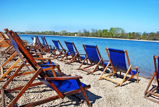 row of  folding chairs by on beach by blue water