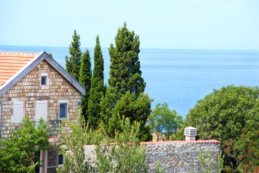 stone house with red tiled roof between cypresses by adriatic sea