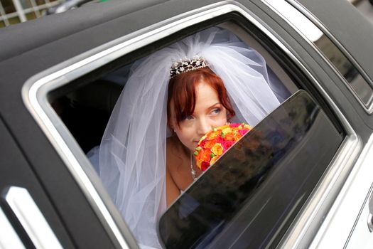 Portrait of smiling bride holding bouquer in wedding car limousine.