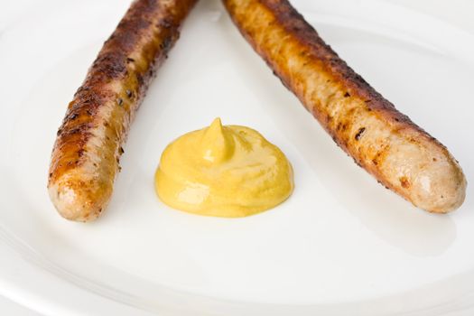 two grilled sausages on a plate with mustard