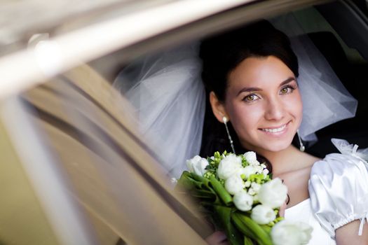 happy bride with flower bouquet siting in the car