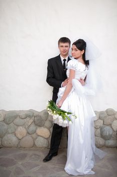bride and groom by the white wall