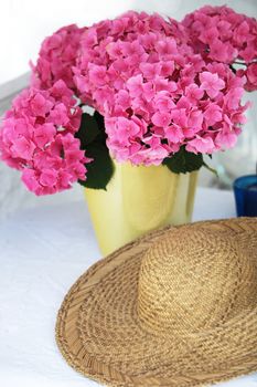 lilac hydrangea in a vase with a straw hat in the foreground