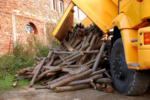 unloading wood delivery from yellow truck by brick house