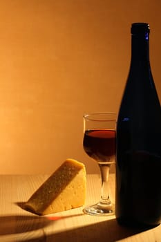 Bottle of red wine, wineglass and piece of cheese on wooden table