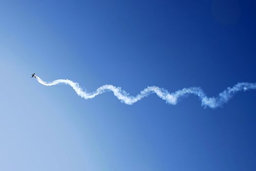 small plane in acrobatic flight with spiral trace over blue sky