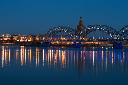 Railway bridge with reflection in river at night. Riga, Latvia.
