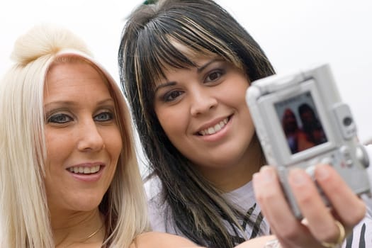 Two young women taking pictures of themselves with a digital camera.