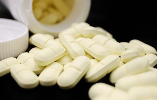 heap of pills and container on black (shallow DOF)