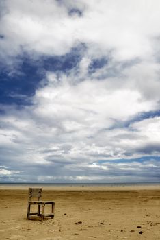 Lonely chair on beach with dramatic clouds.